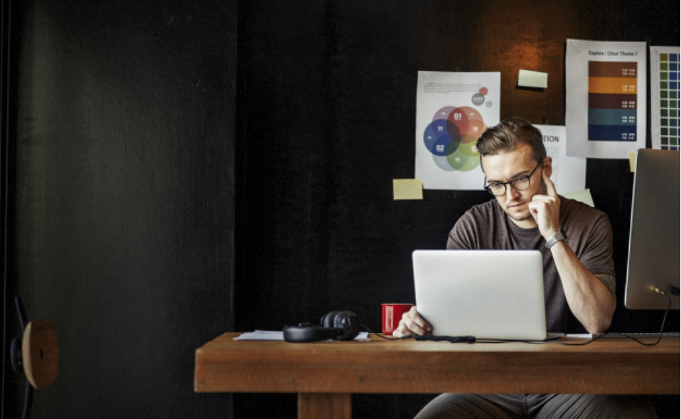 man with glasses using laptop on wood table black walls