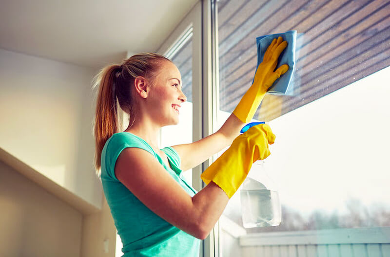 Wiping Windows woman wearing yellow gloves smiling while cleaning windows with blue cloth